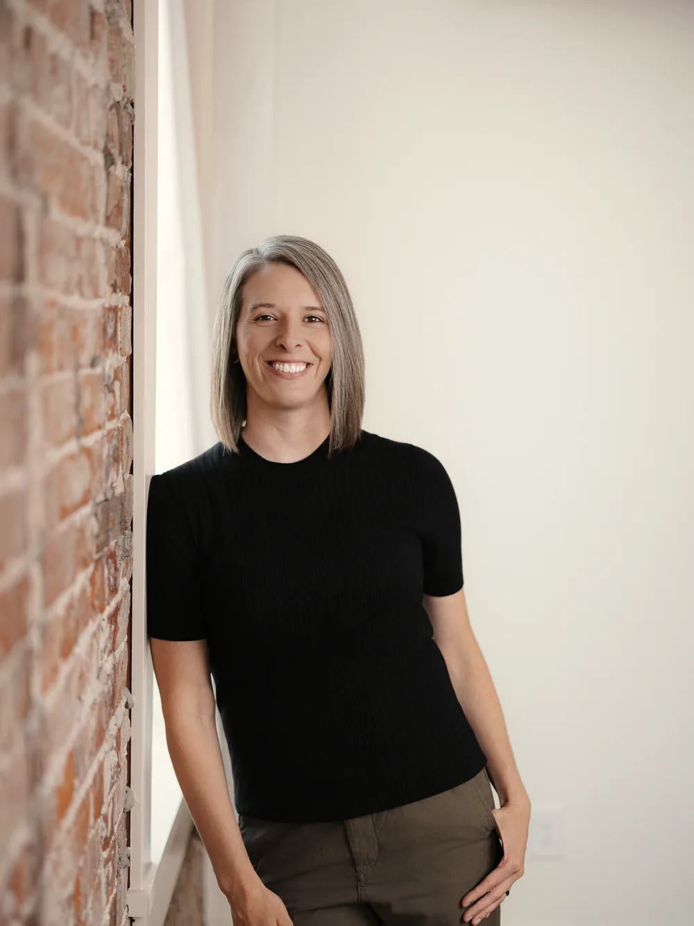 Tasha Francis standing by an exposed brick wall and bright window