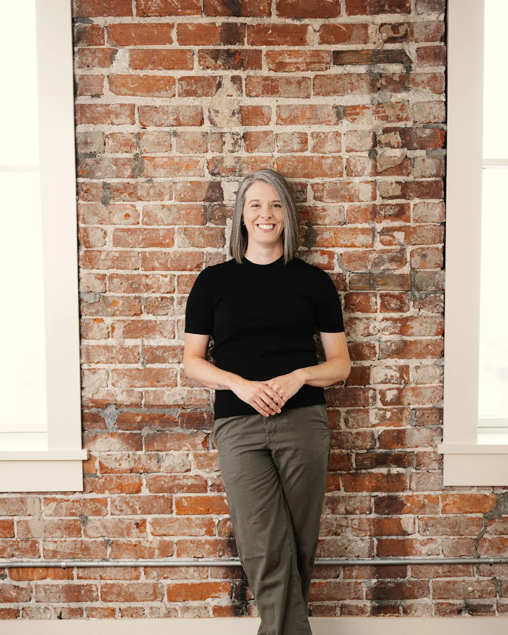Tasha Francis standing against a brick wall in warm window light